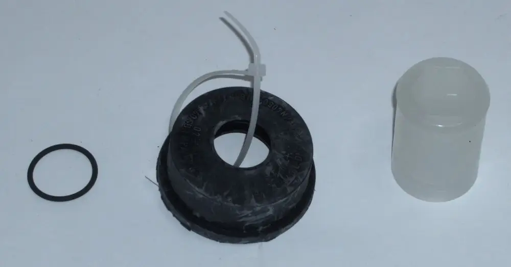 Daikin Schlauchanschluss und Zubehörteile, darunter ein schwarzes Gummi-Element mit mittigem Loch, eine transparente Abdeckung und ein schwarzer O-Ring.